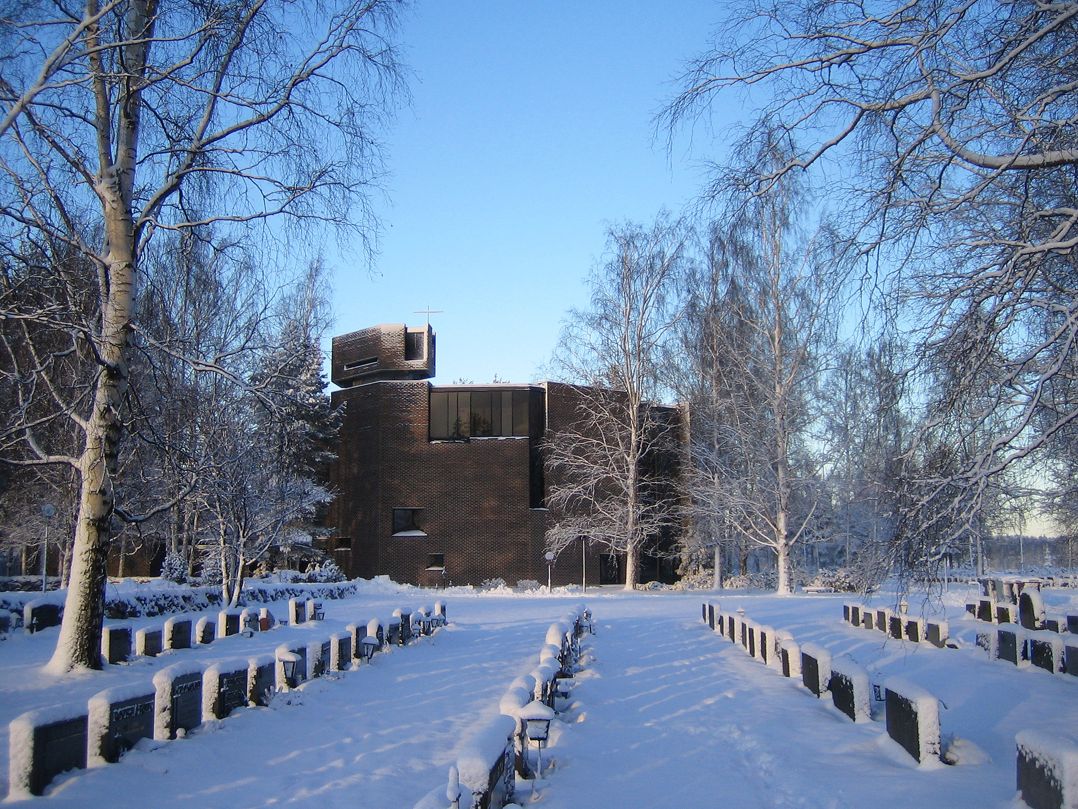 Talvinen kuva, edessä luminen hautausmaa, taustalla Kaikkien Autuuksien kirkko.
