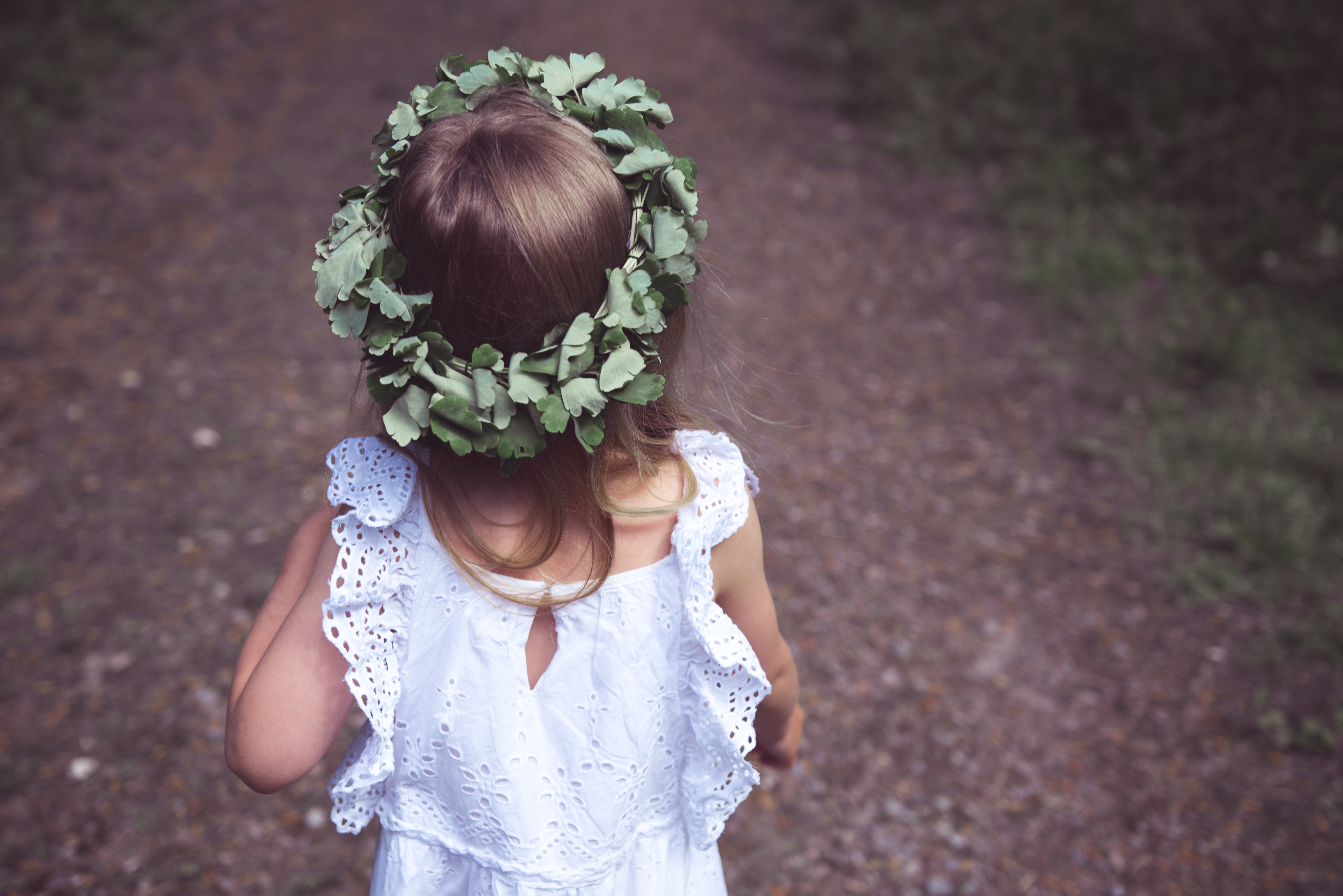 pieni tyttö seisoo selin valkoisessa mekossa ja kukkaseppele päässään